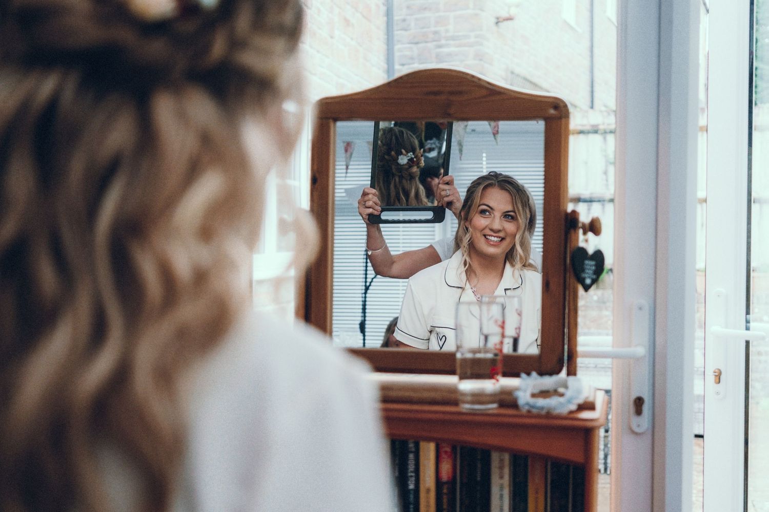 Wedding preparation scene showing a mirror reflection and natural window lighting in a bright interior space.