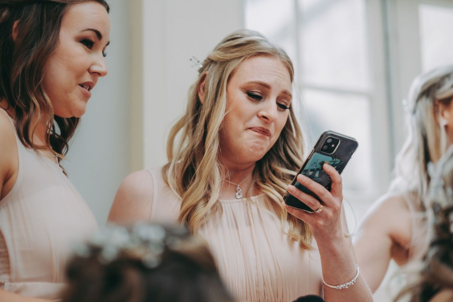 Bridesmaids in matching dresses check their phones during wedding reception.