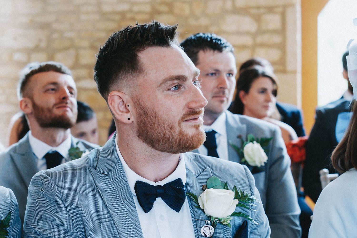 A group in matching grey suits and bow ties share a moment during a wedding celebration.