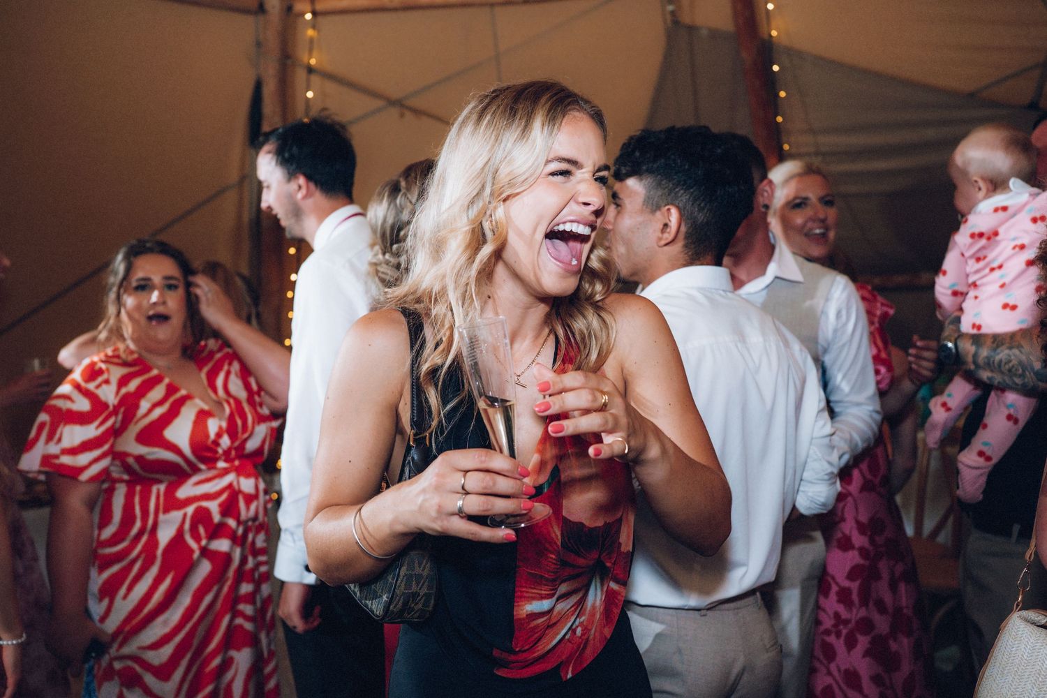 Guests dancing and mingling at a festive wedding reception under warm lighting.