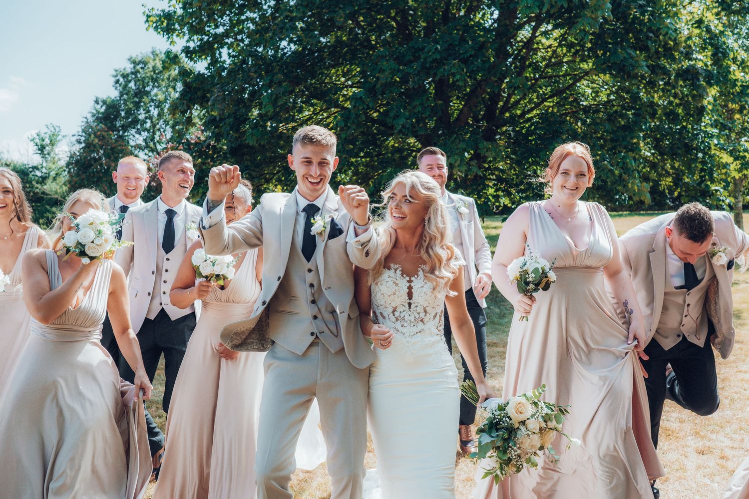 Wedding party celebrates outdoors holding bouquets in coordinated pastel attire.