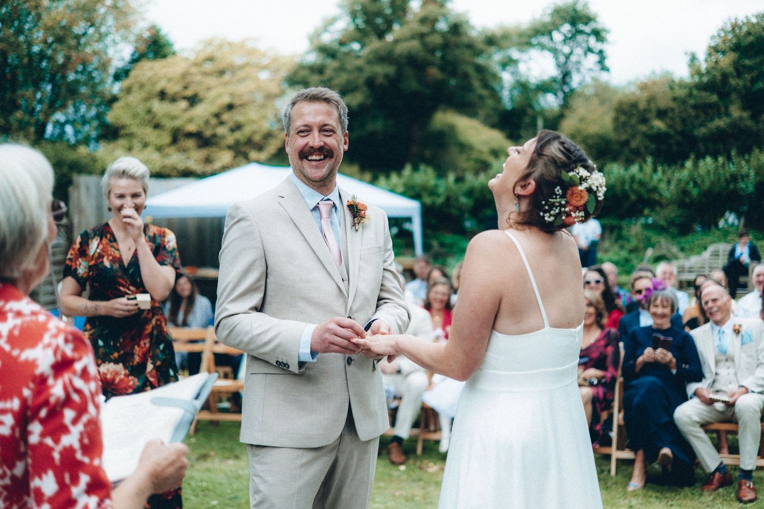Wedding guests watch and smile as the couple celebrates during an outdoor garden ceremony.
