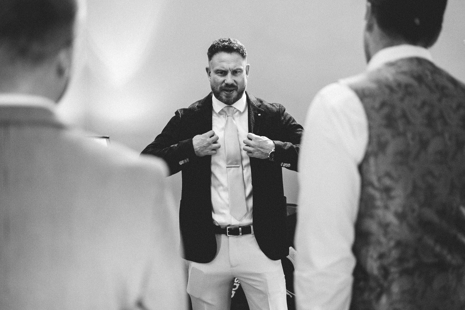 Black and white photo of groomsmen sharing laughs while getting dressed for a wedding.
