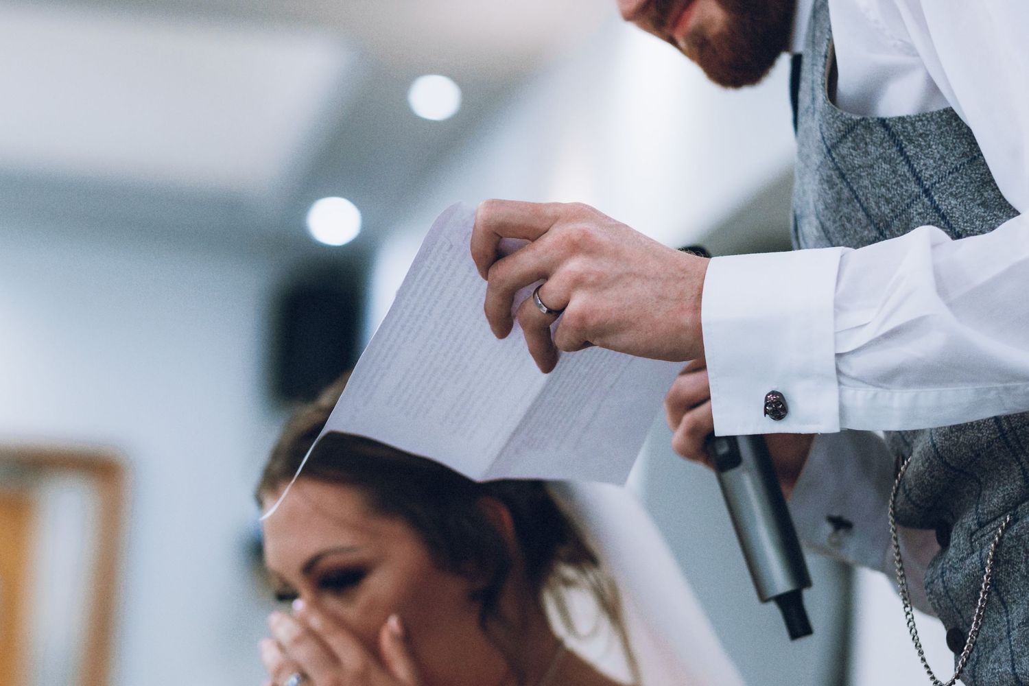 Someone in formal attire reads from papers during a wedding event.