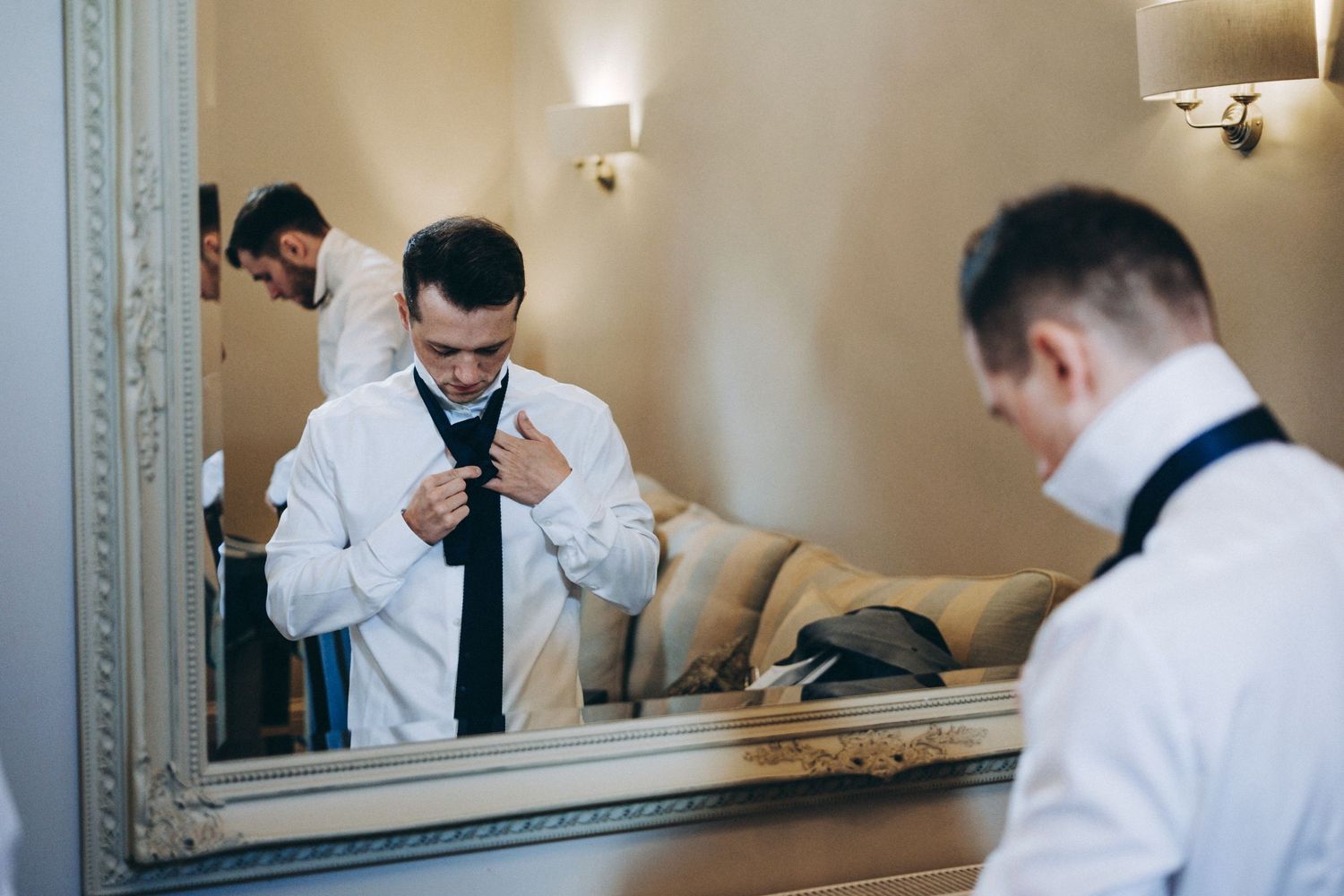 Professional adjusting tie and cuff links while getting ready in front of an ornate mirror.