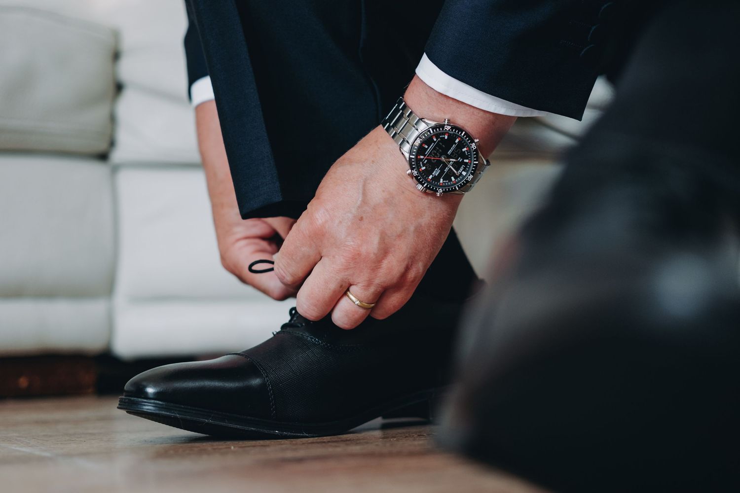 Close-up of hands tying formal black leather dress shoes with luxury watch visible on wrist.