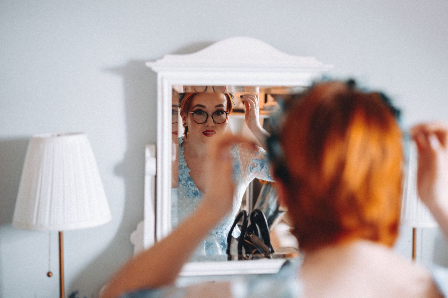 A reflection in a vanity mirror shows the bride styling her red hair ready for her wedding.