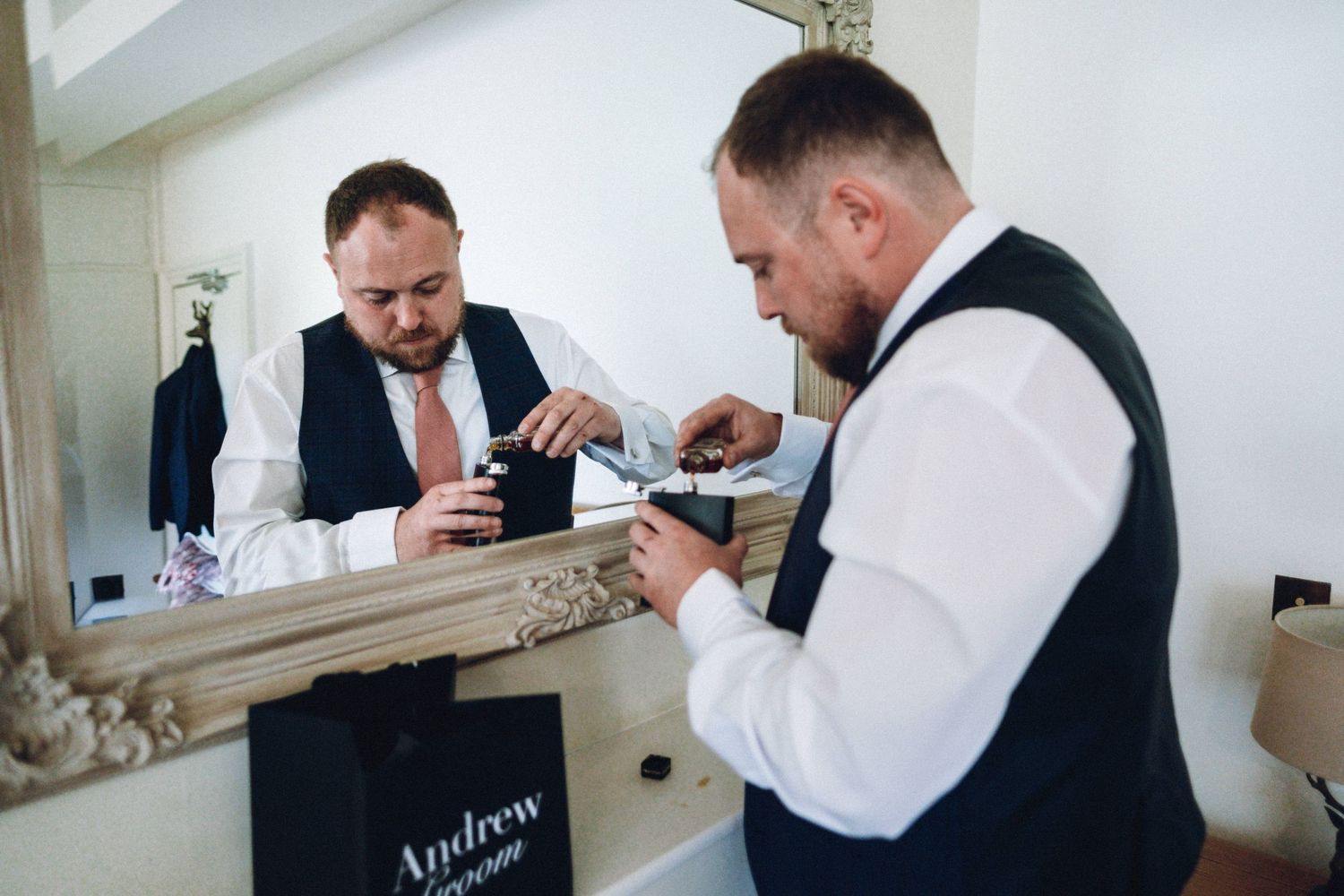 Man in formal attire adjusting his tie in front of mirror.