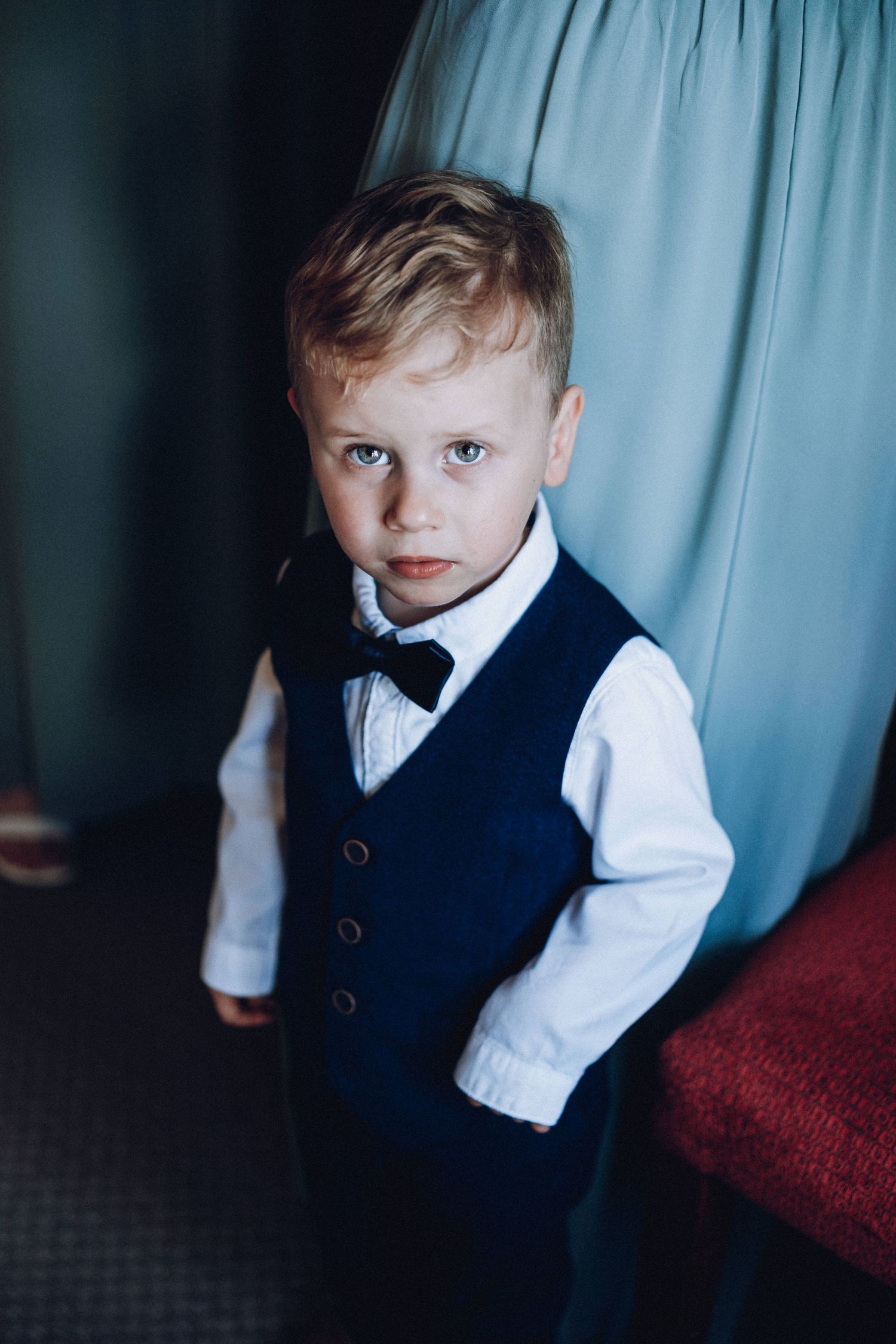 Young boy in navy vest and white shirt posing formally against blue backdrop.