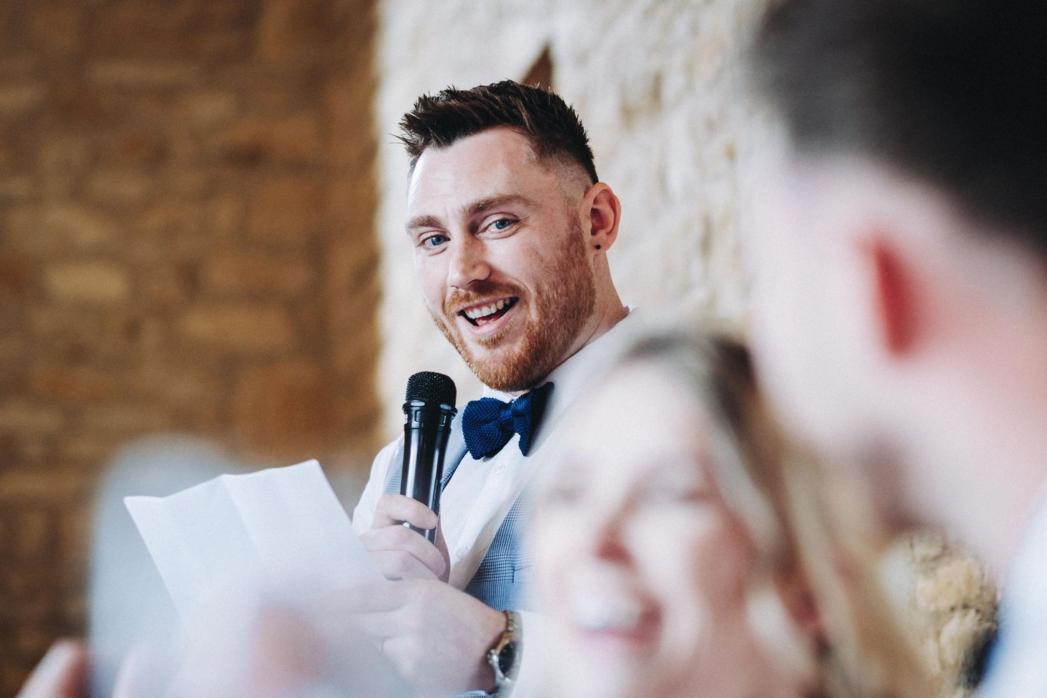 Wedding speeches and toasts being given in rustic stone venue with white decor.