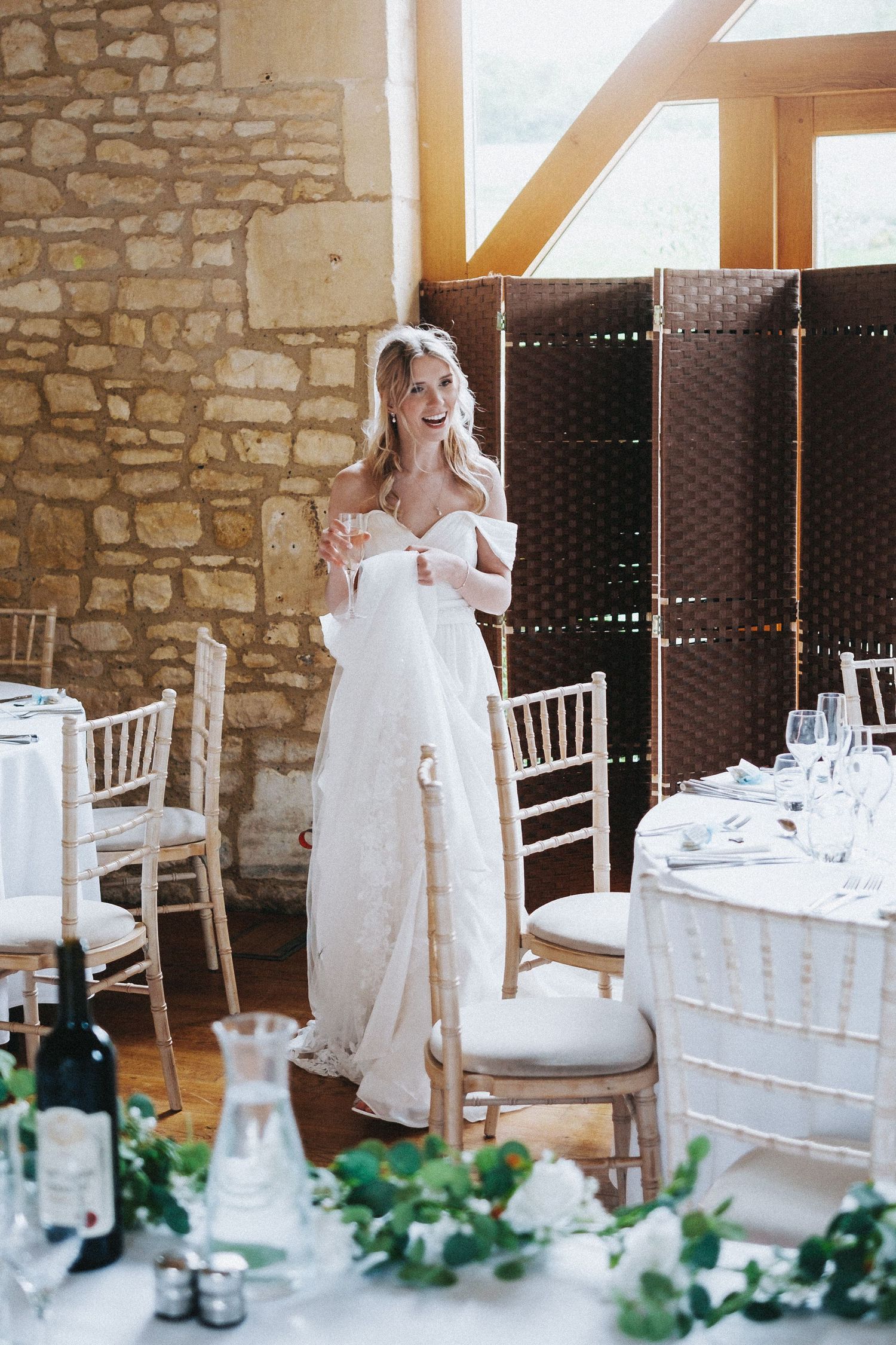 Elegant wedding reception setup with white table settings and greenery garland decor against rustic stone wall interior.