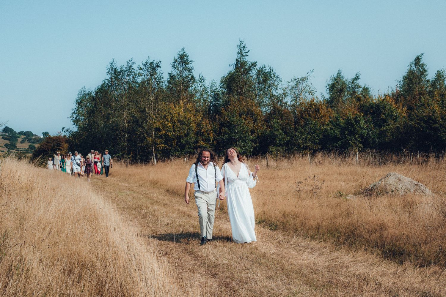 People walking along a dirt path through a golden grass field.