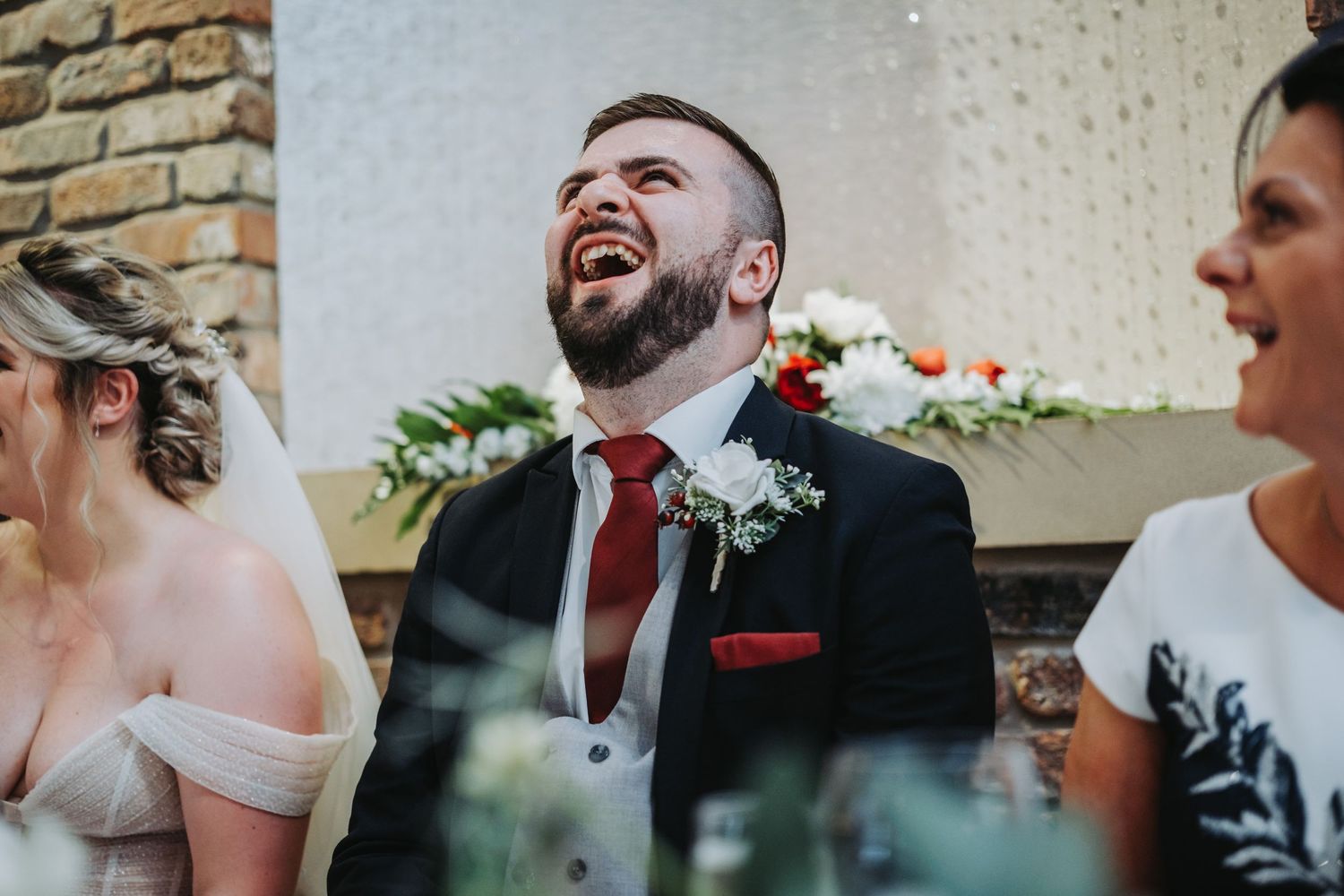 A candid moment of joyful laughter at a wedding celebration with a red tie and boutonniere.