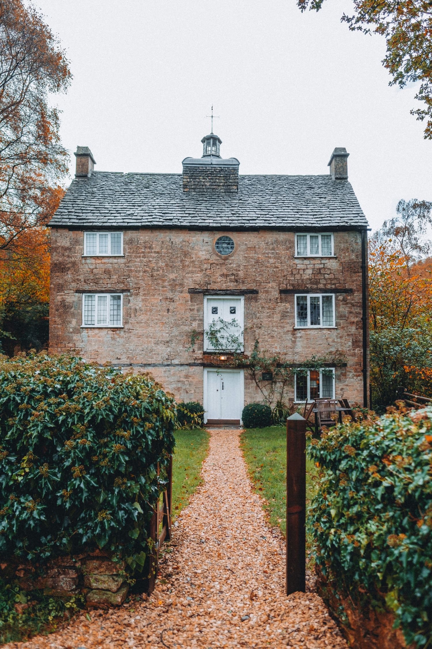 Stone cottage with slate roof and hedged pathway covered in autumn leaves.