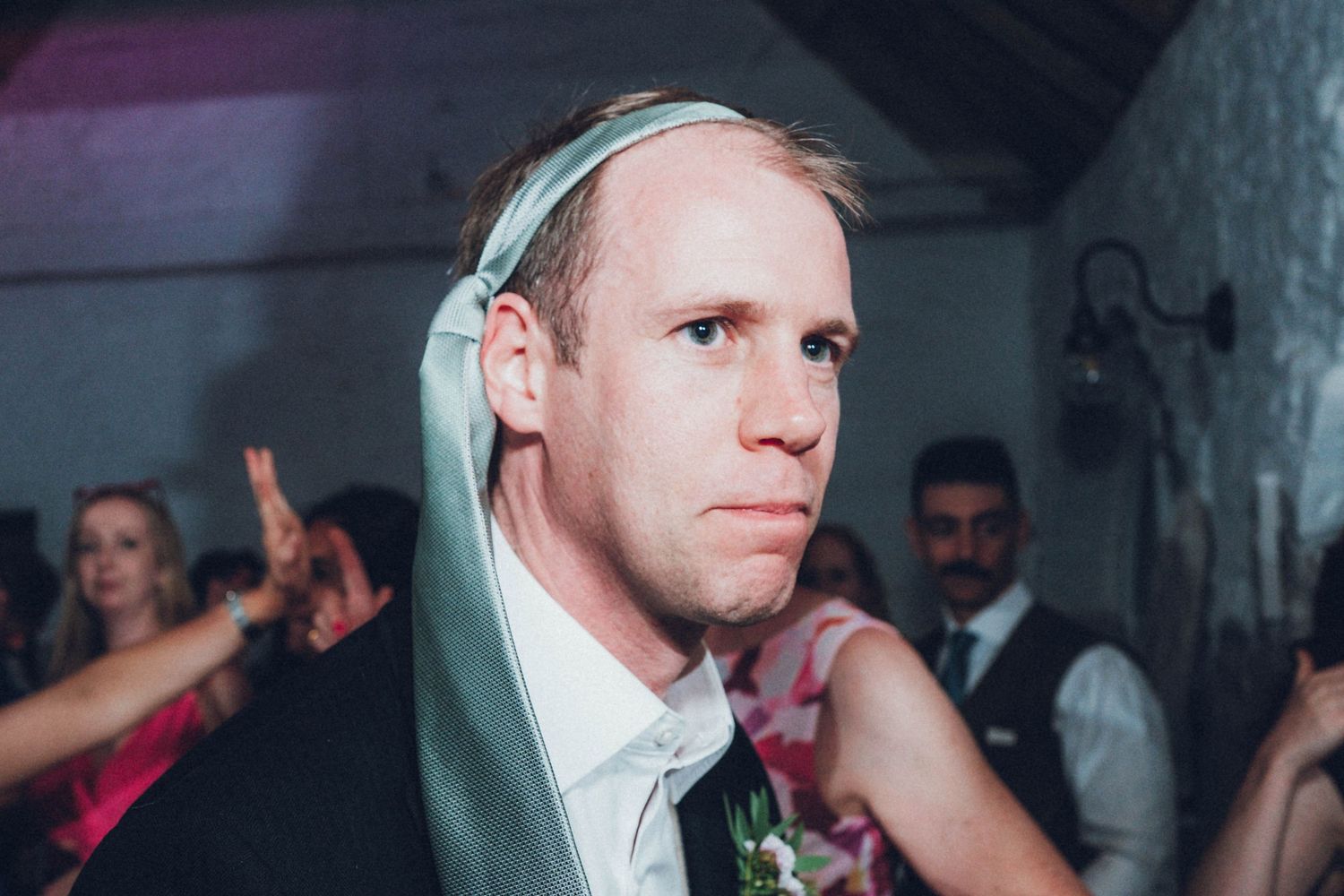 Party guests dancing and celebrating at a dimly lit wedding reception.