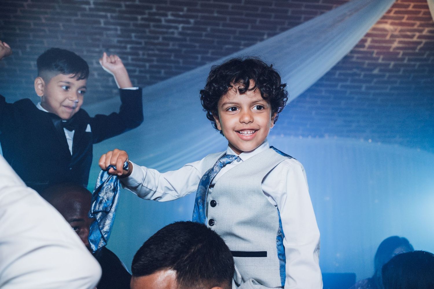 Guests dancing and celebrating at a wedding reception under blue mood lighting.