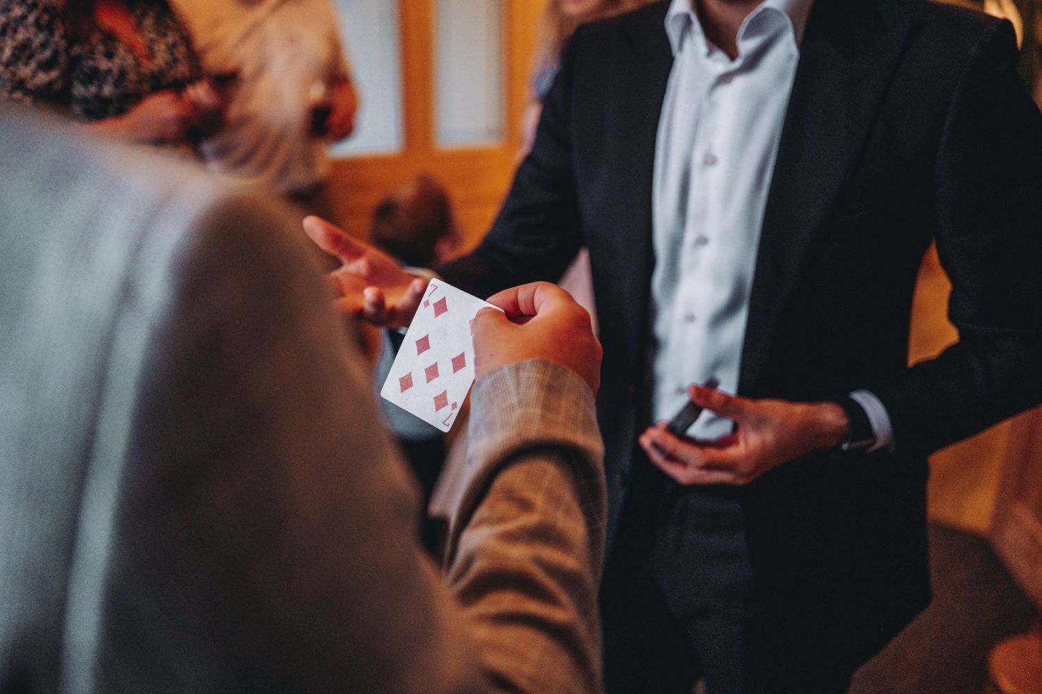 Close-up view of someone performing a card trick while wearing a black suit jacket during an indoor entertainment event.