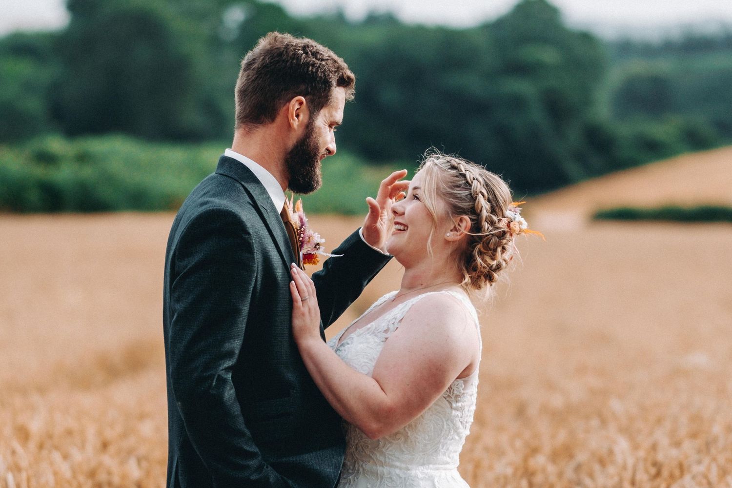 A joyful wedding couple shares a candid laughing moment together in a golden wheat field at sunset.