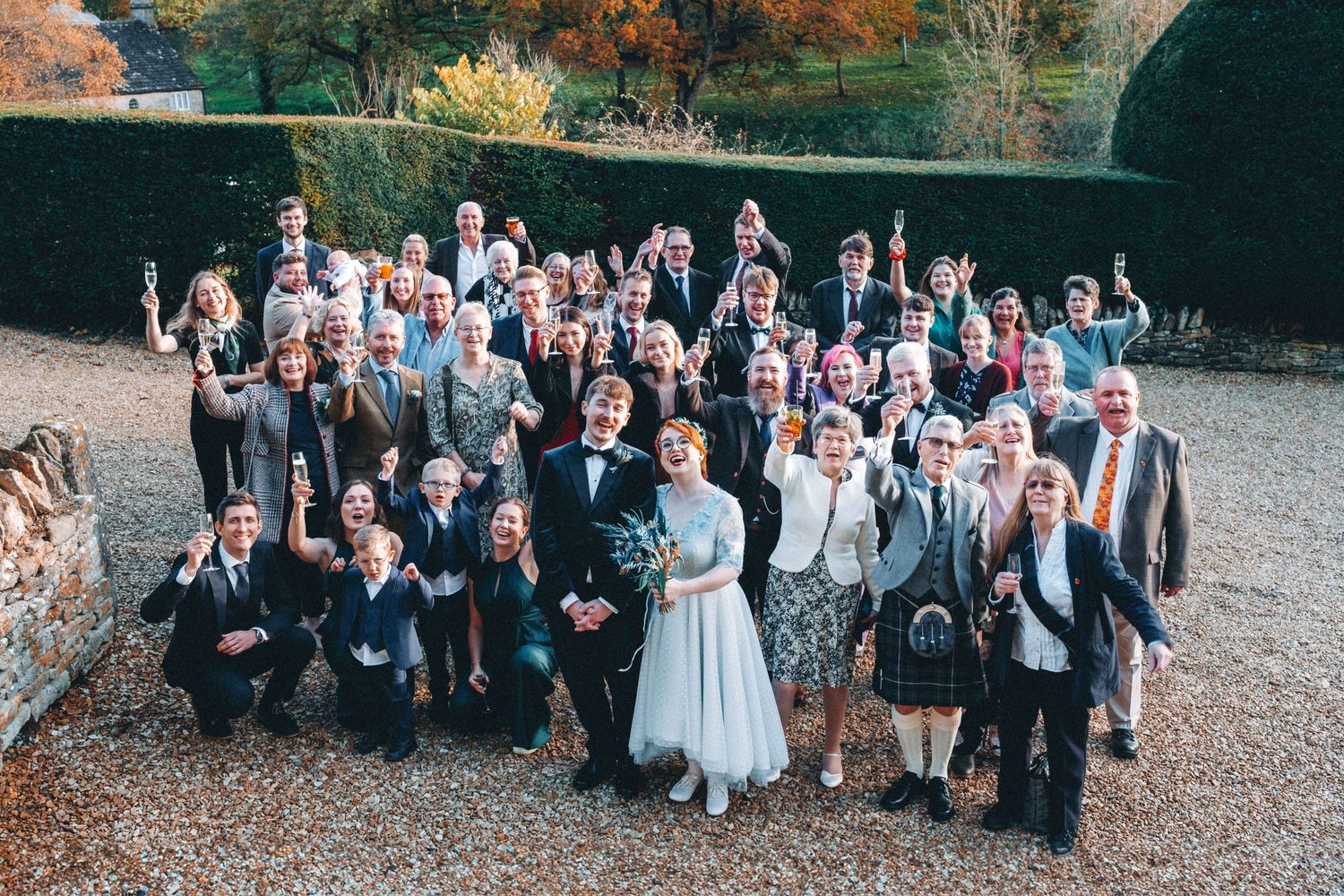 Large wedding group photo with guests gathered outdoors in formal attire.