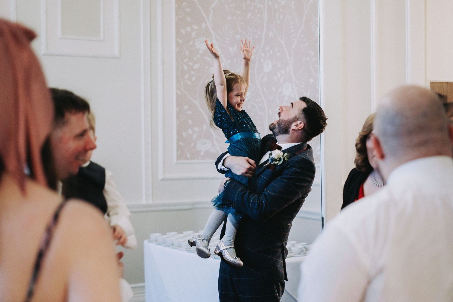 Wedding guests share emotional embraces during celebration in white interior room.