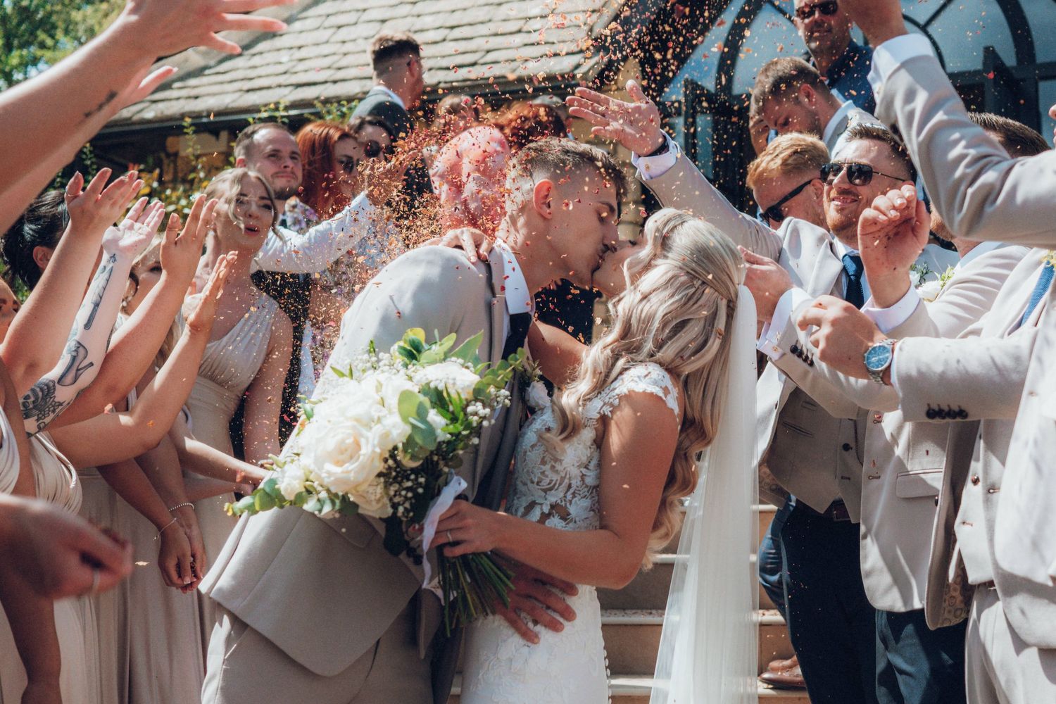 Wedding guests throw confetti over the newlyweds during outdoor celebration.