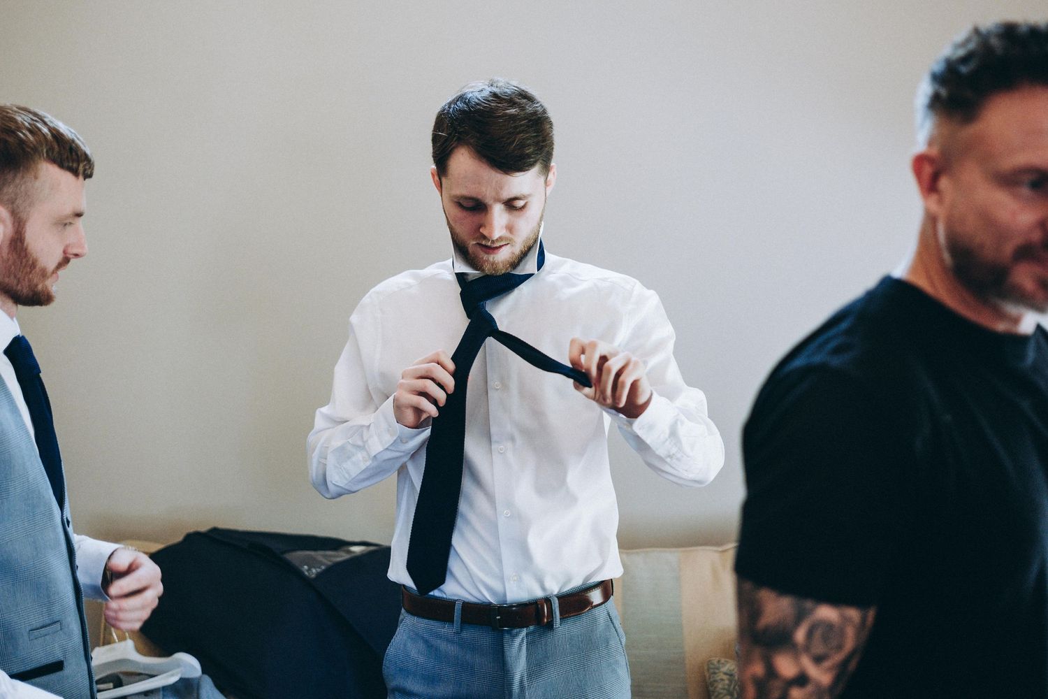 Groomsmen in formal attire getting ready and helping each other prepare for a wedding ceremony.