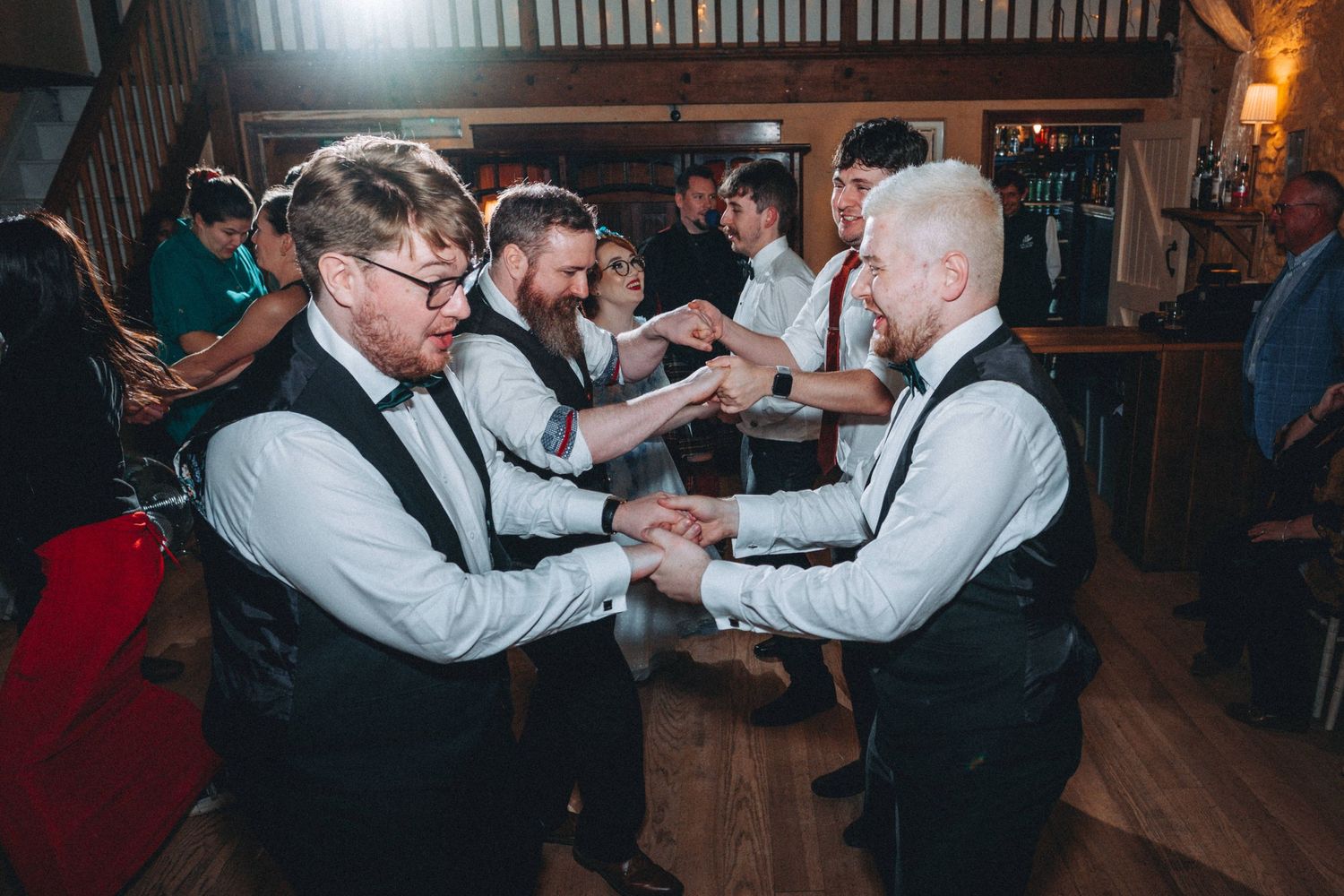 Wedding guests dancing together on wooden floor during reception celebrations.