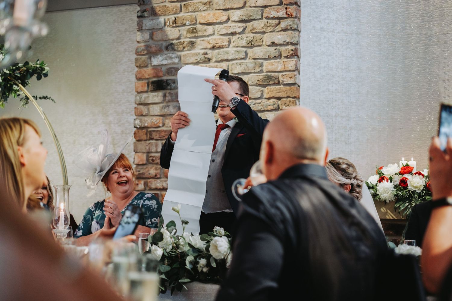 Wedding guests laugh and celebrate during a reception toast at a venue with stone brick walls and table decorations.