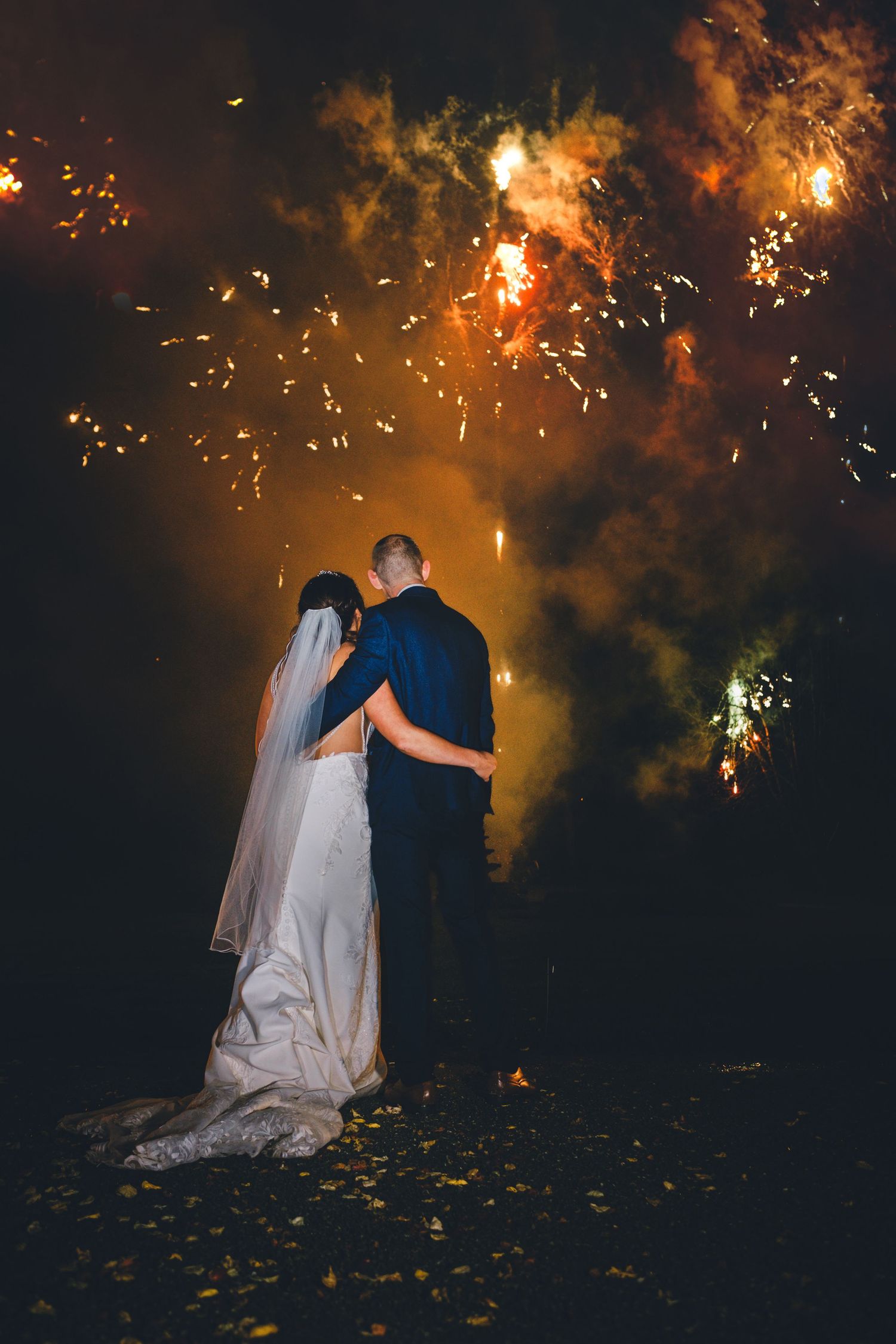 Romantic silhouette of newlyweds against dramatic fireworks display at night.