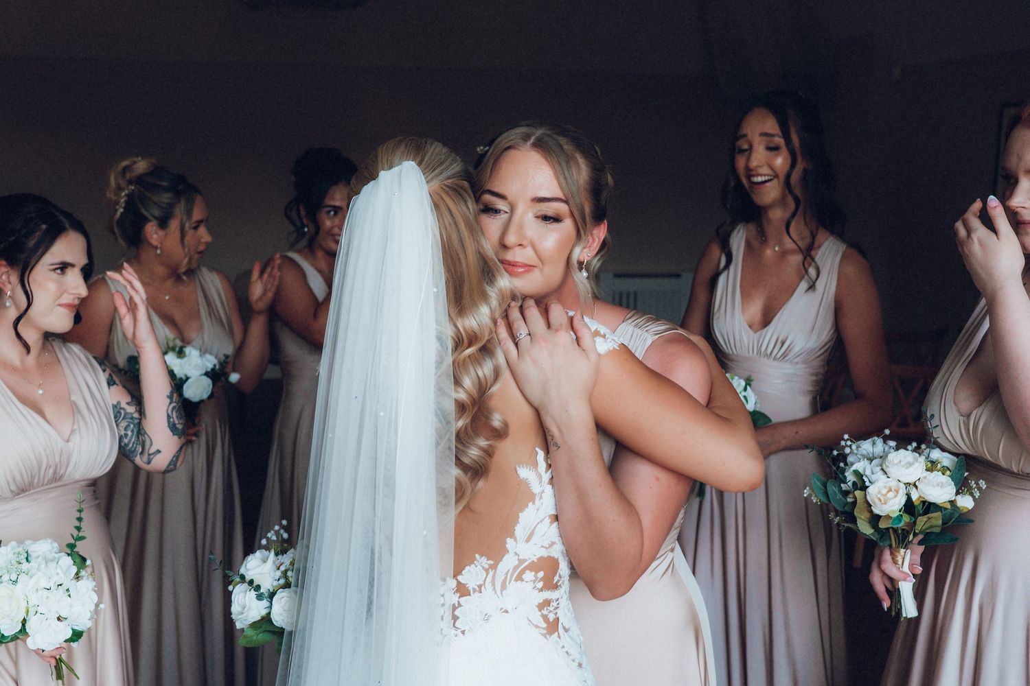 Wedding party in blush colored dresses sharing emotional moment together.