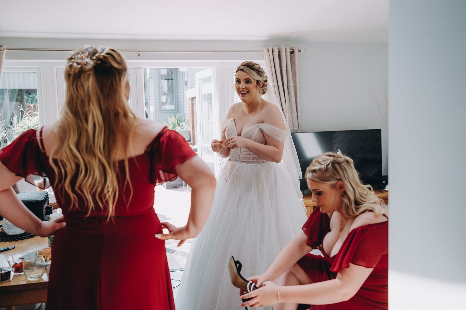 Wedding preparation scene with attendants in red dresses helping with final touches.