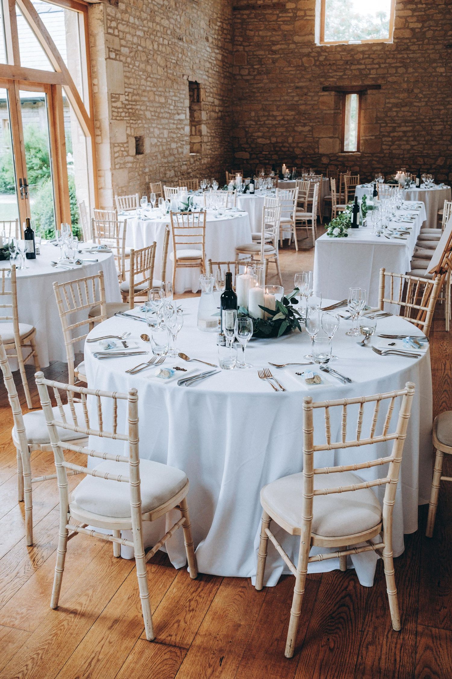 Rustic wedding reception venue with white round tables, chiavari chairs and exposed brick walls in natural lighting.