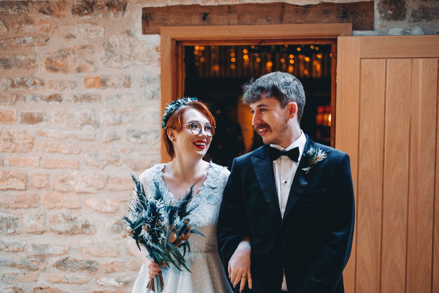 A joyful couple share a tender moment against a rustic stone wall backdrop at their vintage-style wedding.