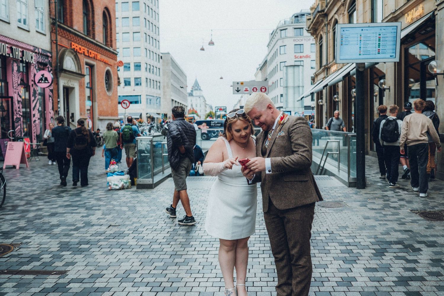 Couple walking down busy city street with historic buildings and shops.