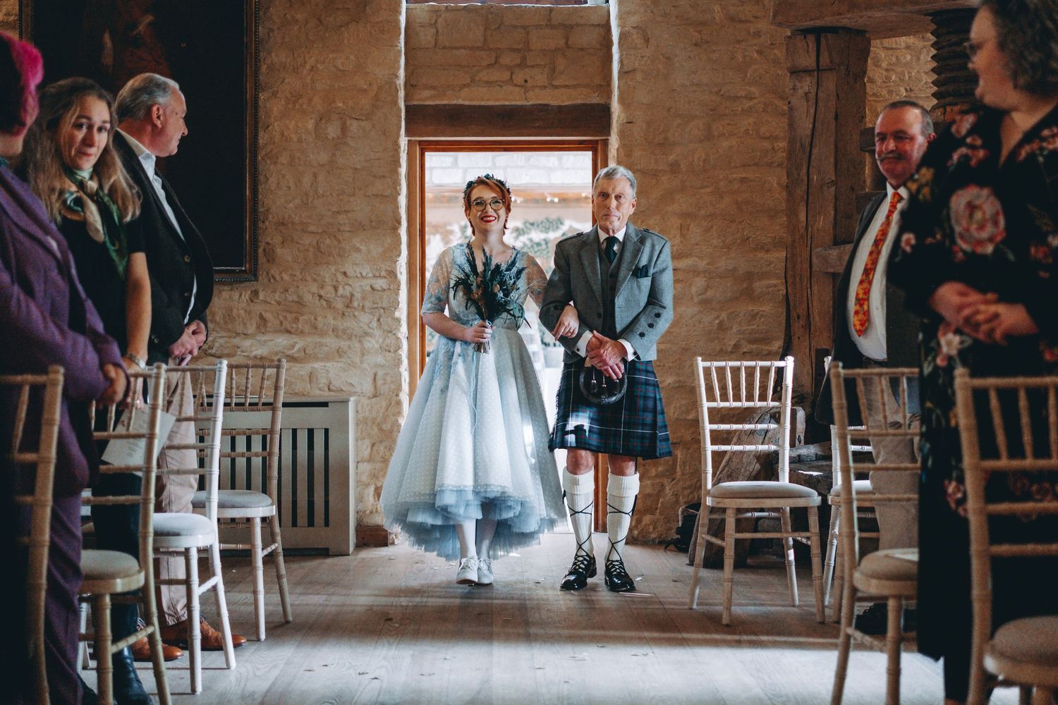 A couple enters their wedding ceremony through rustic stone doorway as guests look on.
