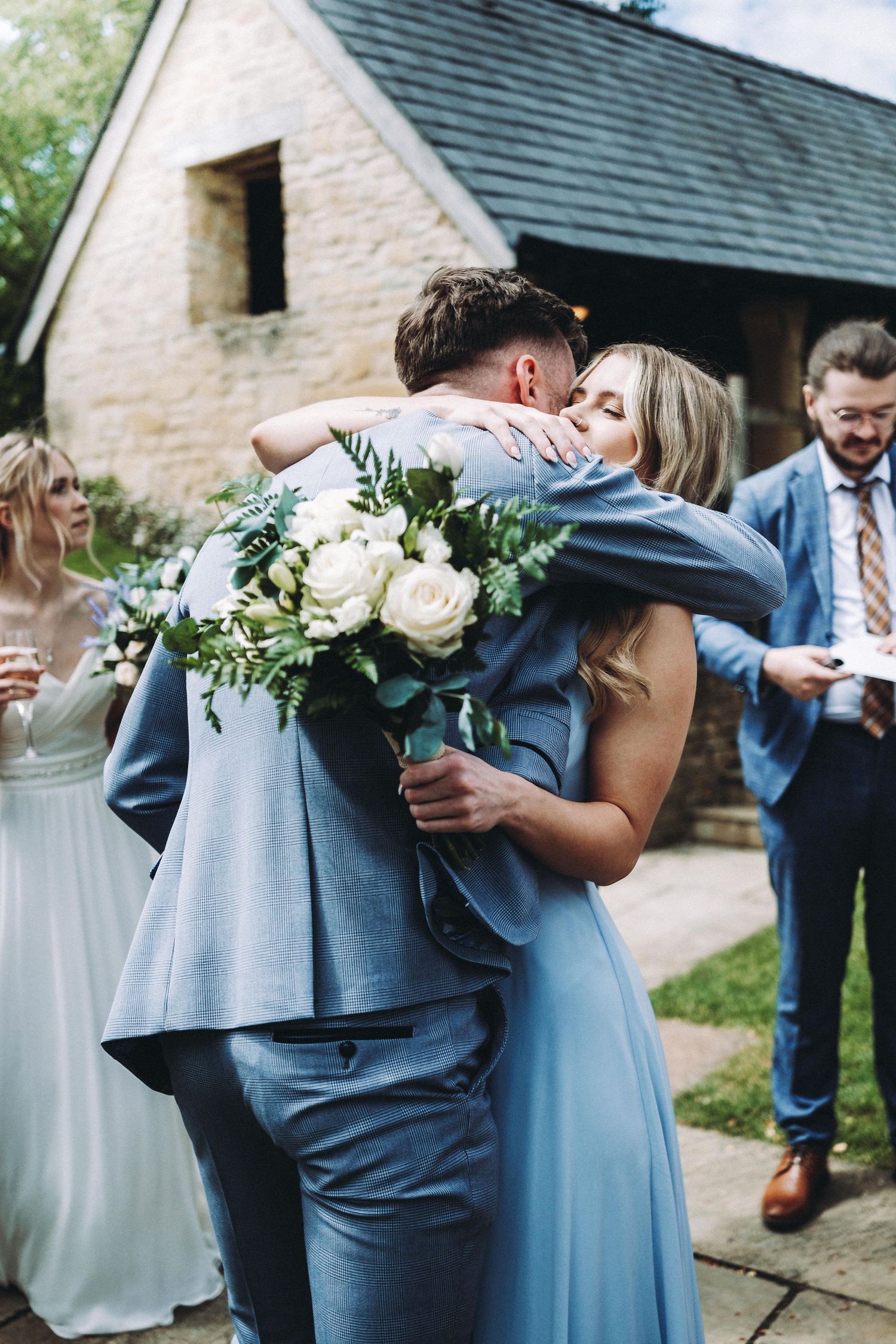 A tender embrace between wedding attendees with a bouquet of white roses.