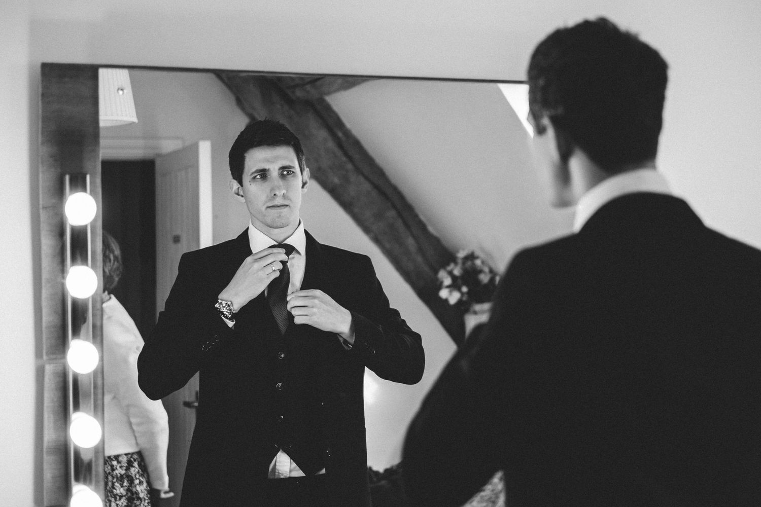Black and white reflection of formal attire adjustments in a mirror.