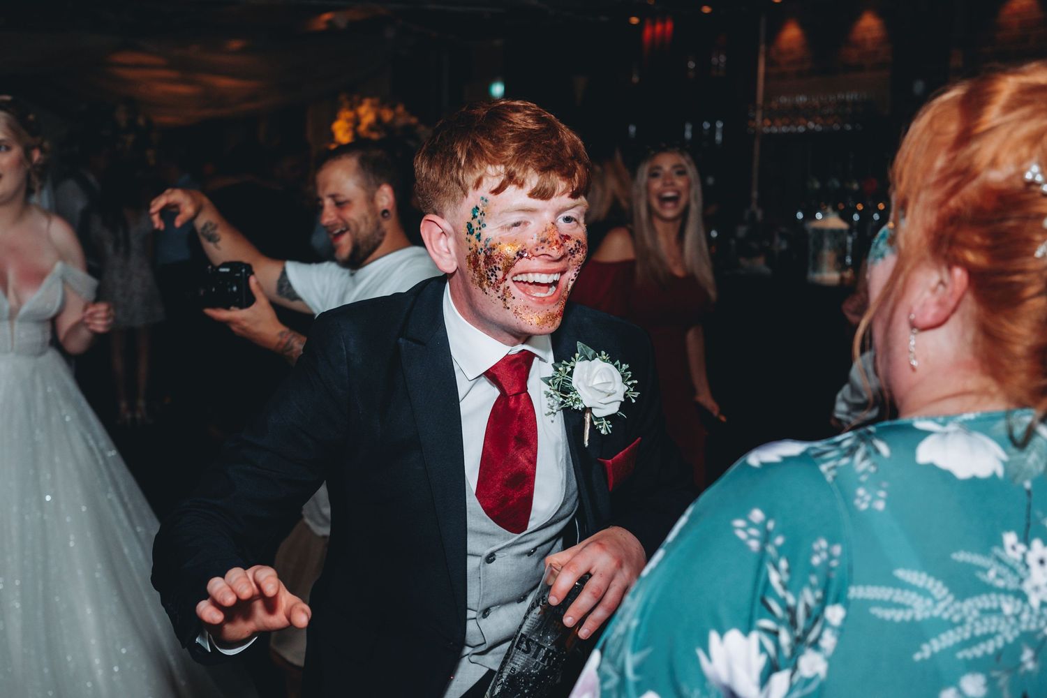 Wedding guest in formal black suit and red tie dances energetically on the reception dance floor.