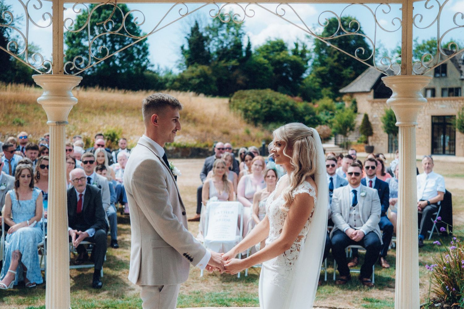 Garden wedding ceremony with white chairs and ornate pillars creating a romantic aisle.