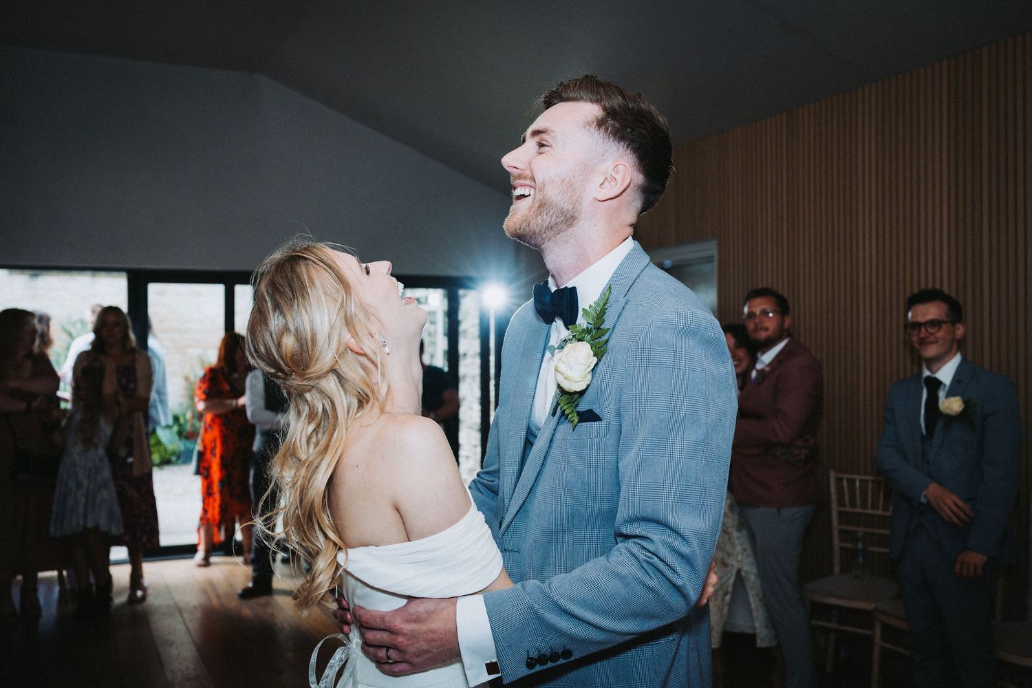 Wedding reception guests dance and celebrate in a dimly lit indoor venue.