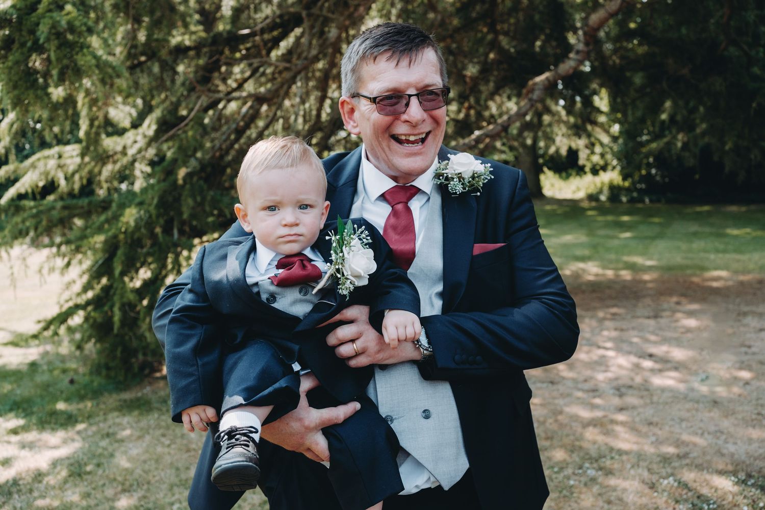 Formal wedding attire and boutonniere details captured outdoors in natural garden setting.