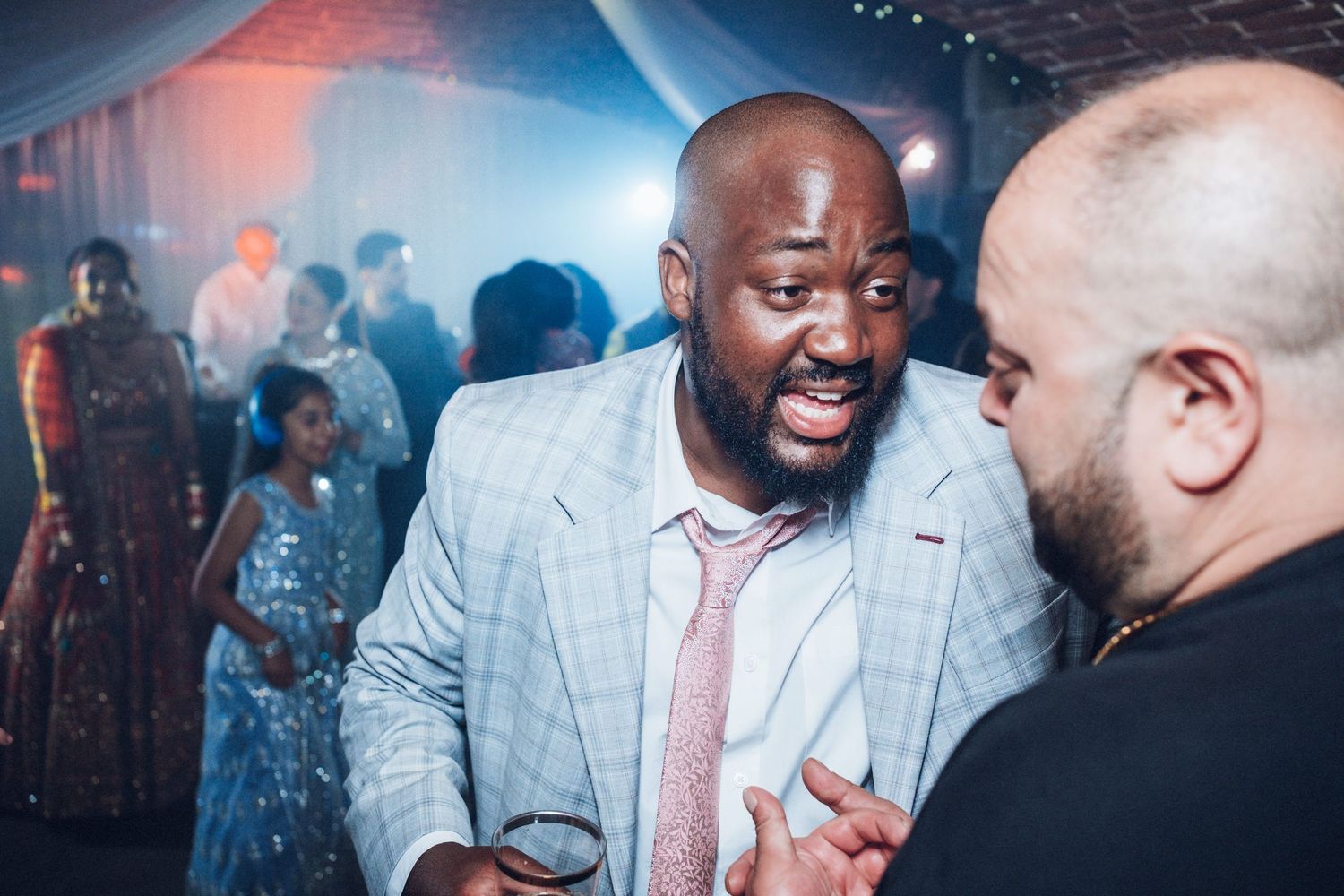 Wedding guests mingling and socializing under atmospheric lighting at an indoor venue.