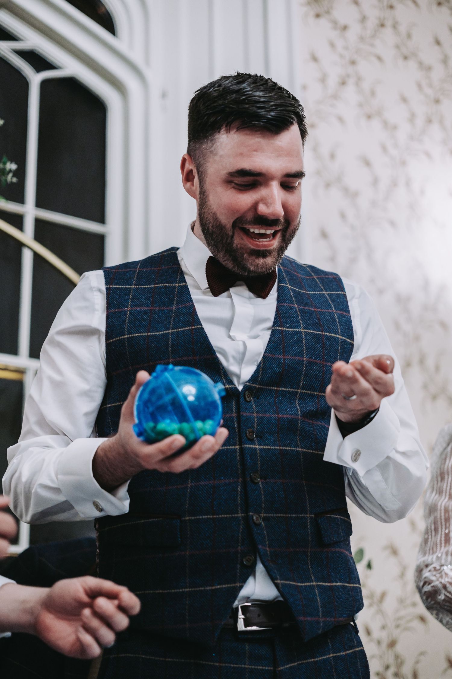 Guest in checkered vest holds blue bowling ball during wedding reception.