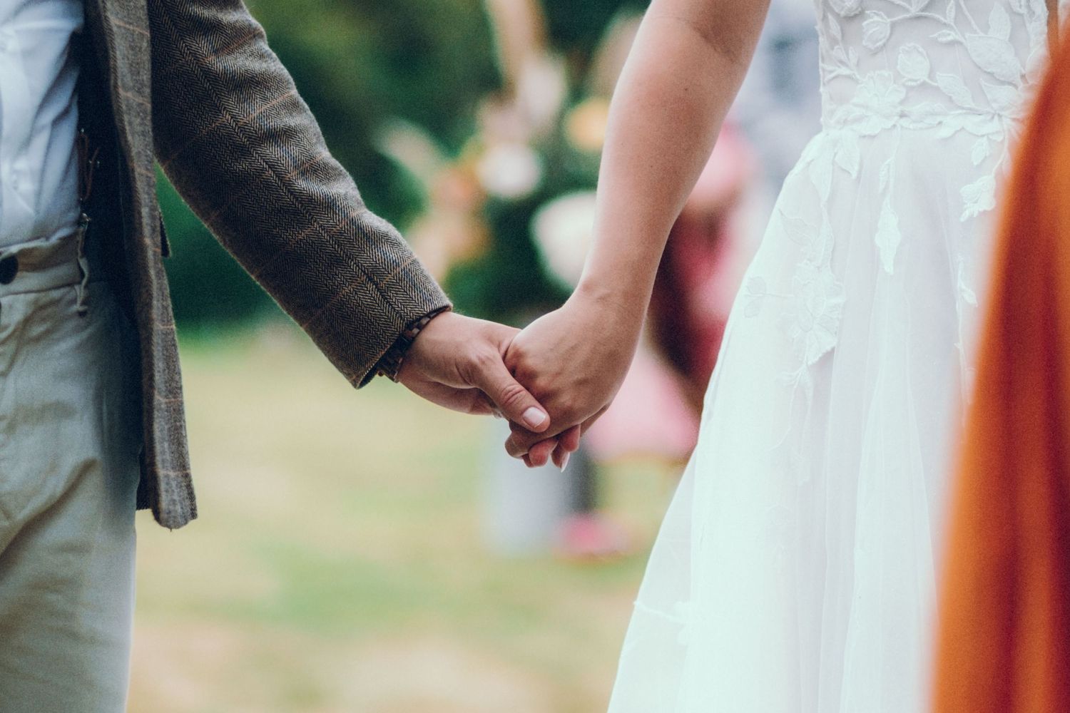 Close-up shot of couple holding hands during outdoor wedding ceremony.