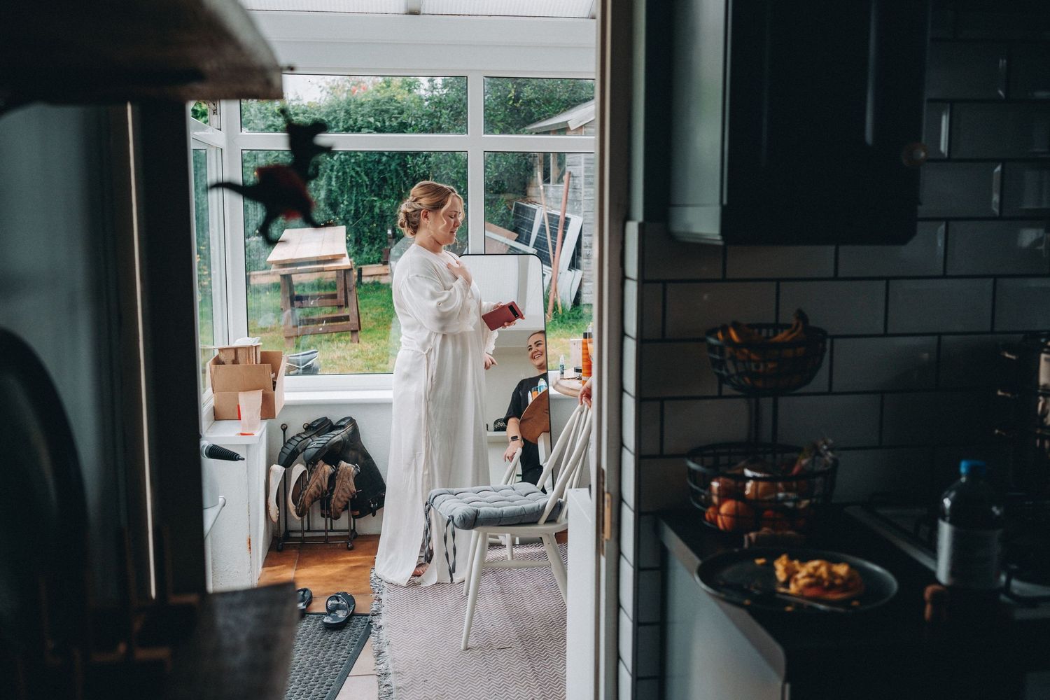 View through doorway of sunny screened porch with bride in white dressing gown getting ready for bridal prep.
