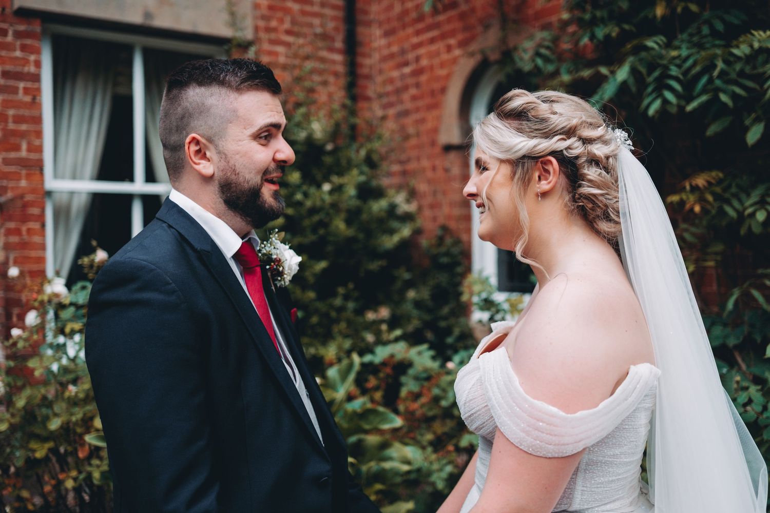 Elegant wedding portraits against brick building with lush garden backdrop.