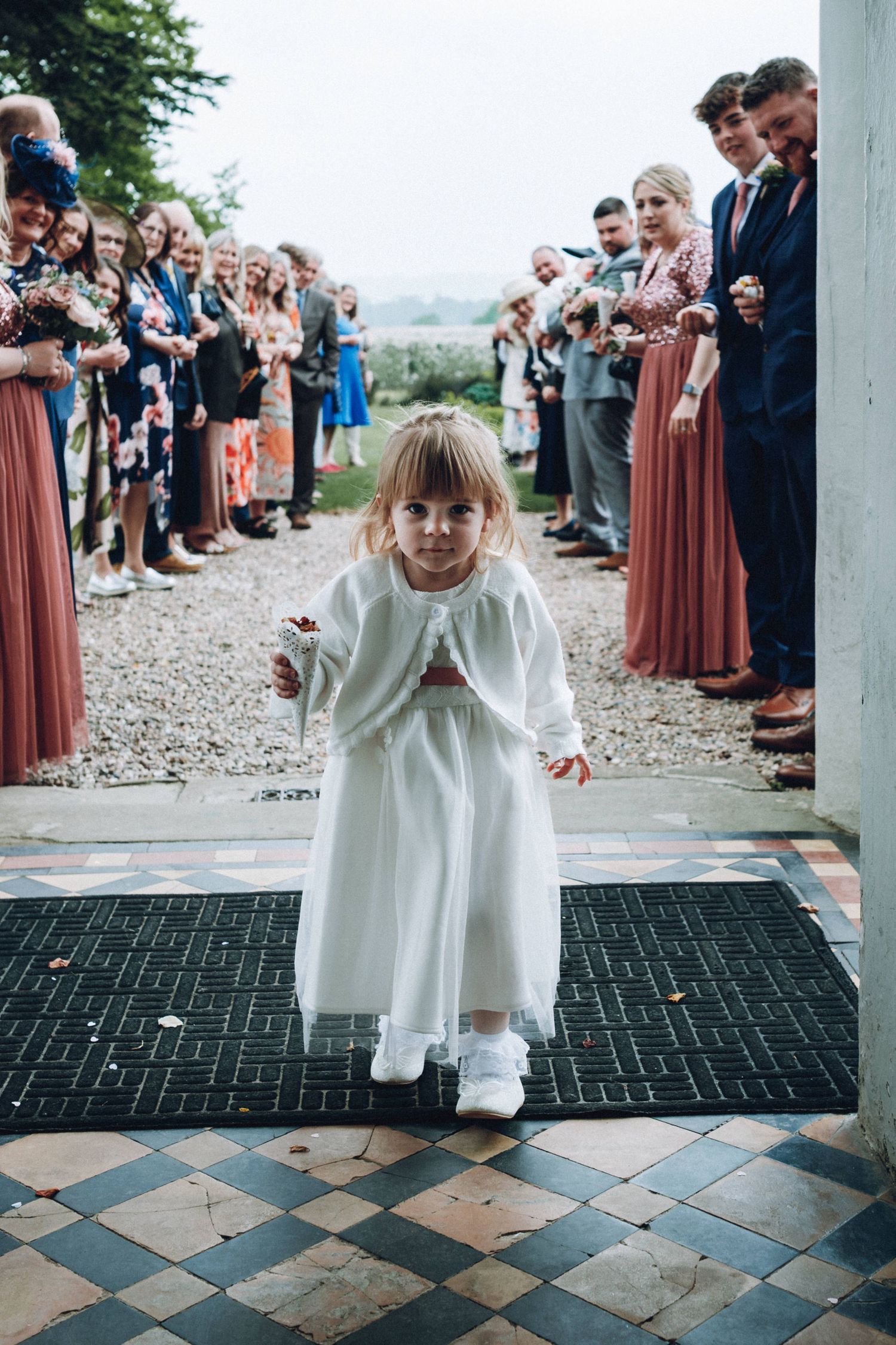 Children in white dresses stand on a checkered floor at a wedding venue entrance.
