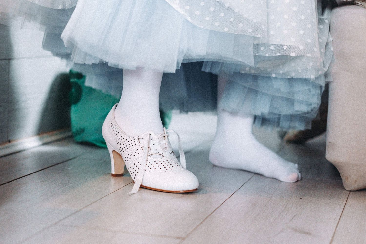 White vintage-style bridal shoes with heels shown against layers of tulle dress fabric.