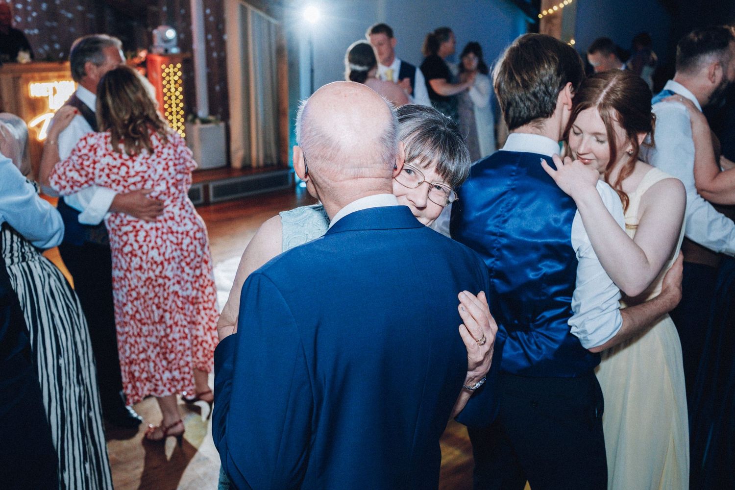 Wedding reception guests dancing and celebrating in a dimly lit venue.