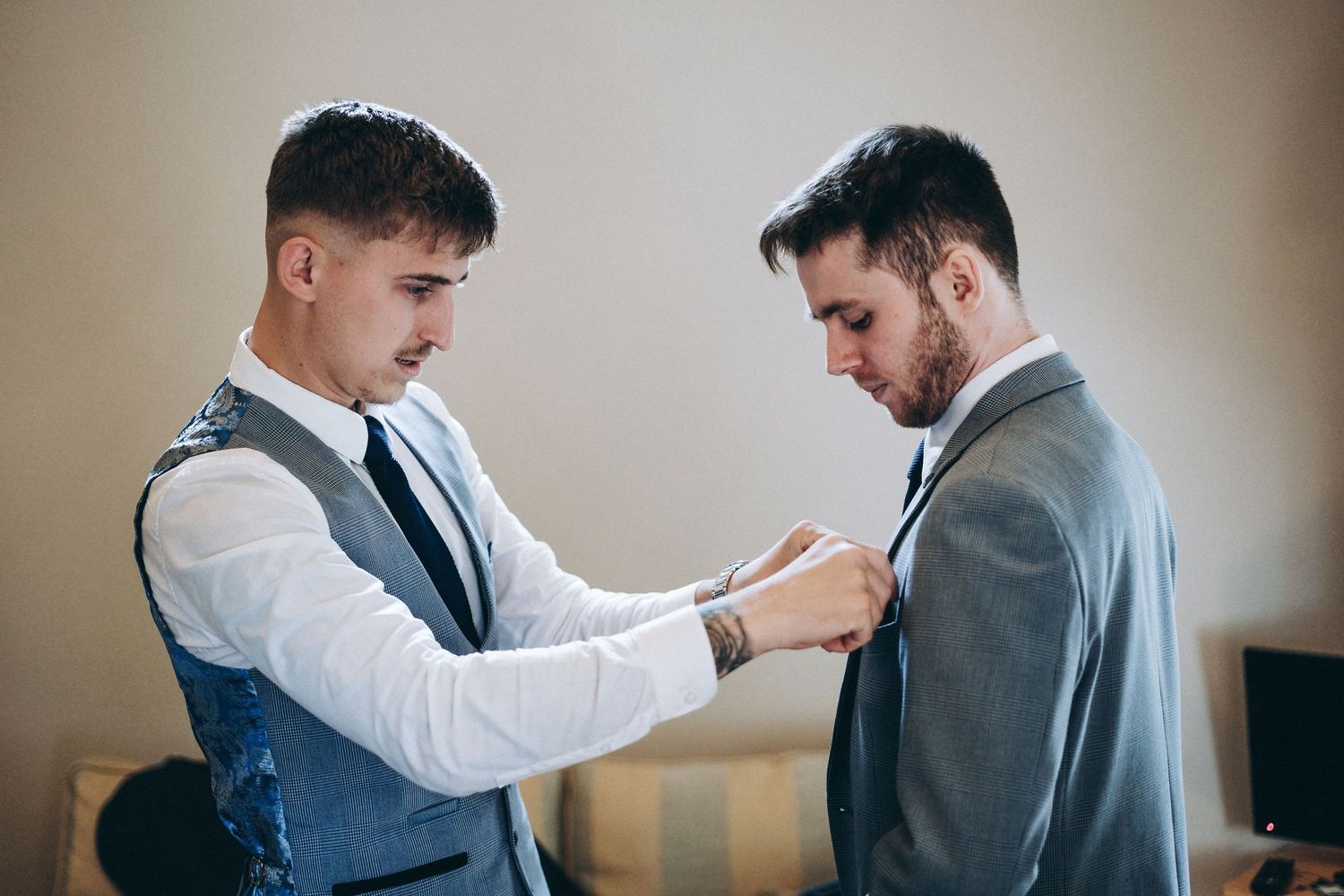 Groomsmen assisting with formal wear adjustments in a hotel room before the ceremony.